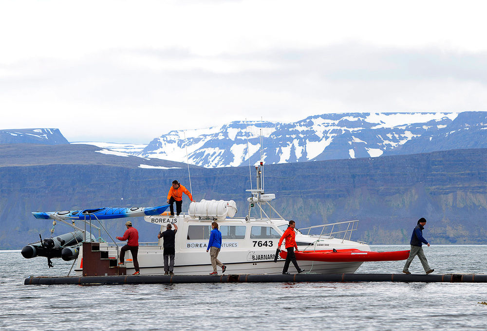 People Carrying Kayaks Off The Boat With Mountains In The Background in Iceland