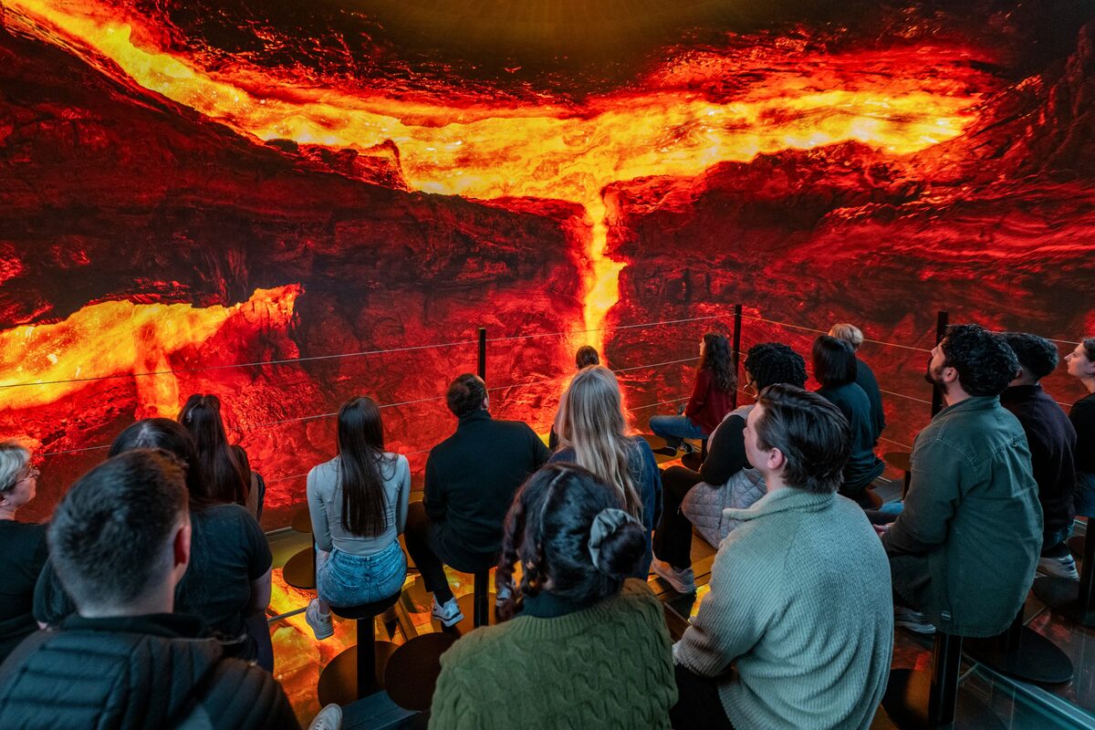 Audience on stools watching wall-sized lava footage at Perlan's Volcano Show in Reykjavík.