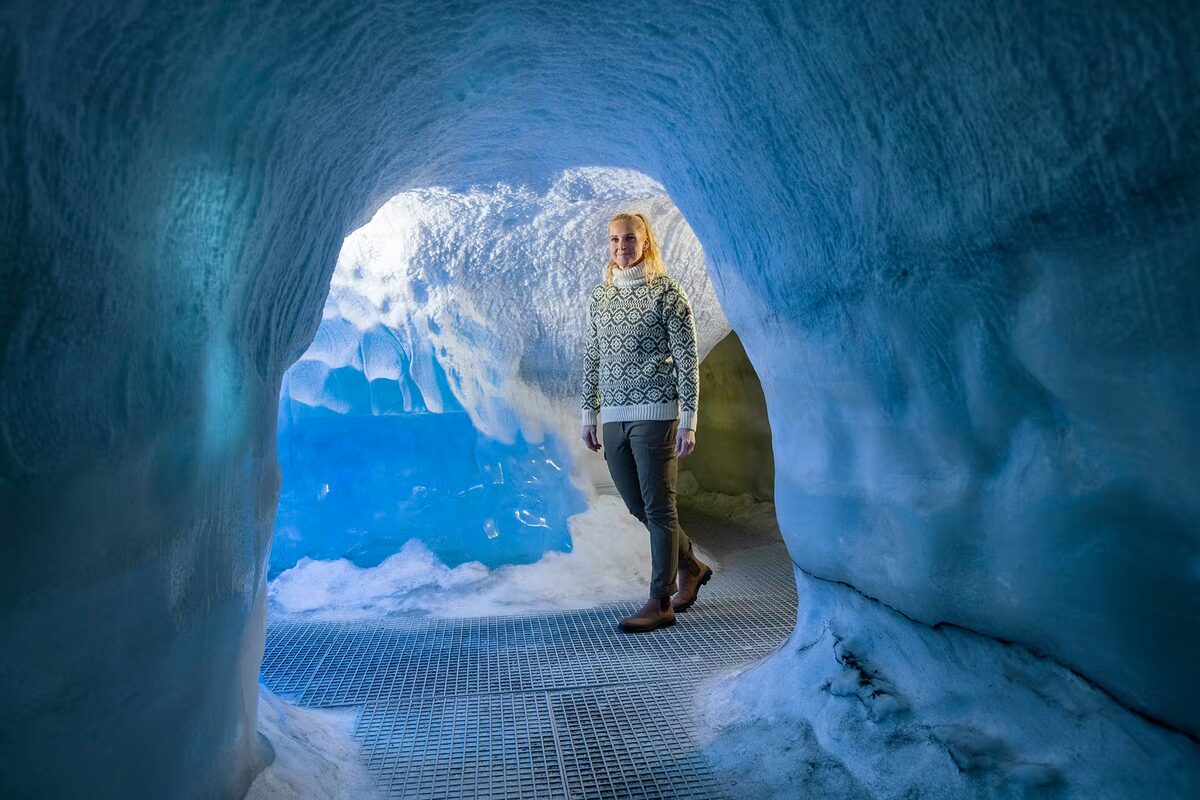 Visitor in a patterned wool sweater inside Perlan's blue-lit indoor ice cave on a metal walkway.