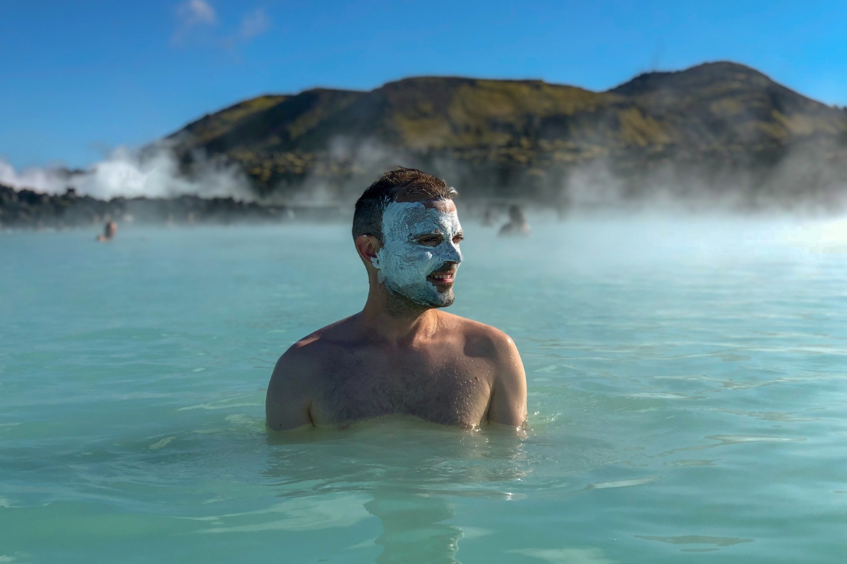 Visitor with silica mud masks soaking in the Blue Lagoon as steam rises over the water.