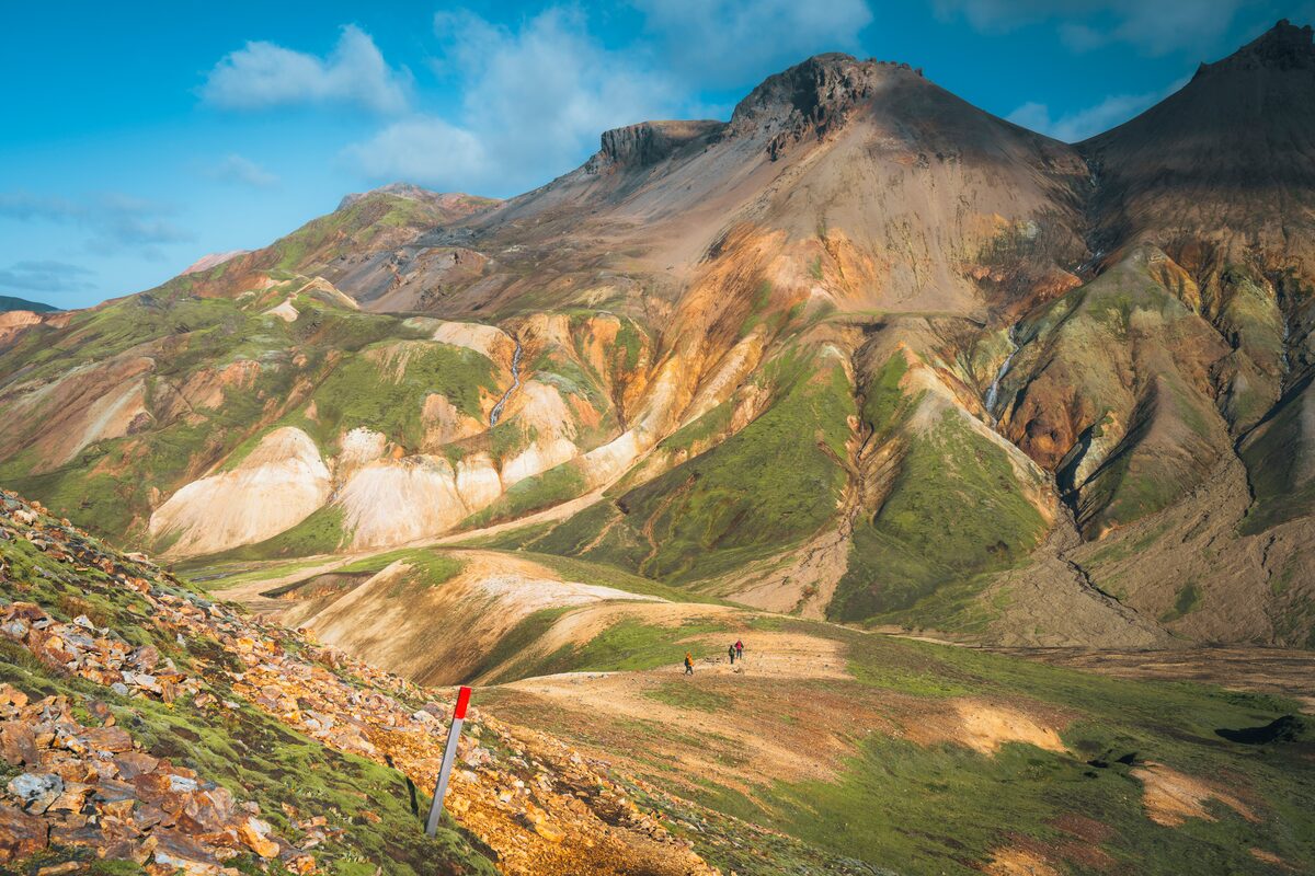 Rhyolite mountains in orange, green, and beige at Landmannalaugar in the Icelandic Highlands, hiker on the trail for scale.