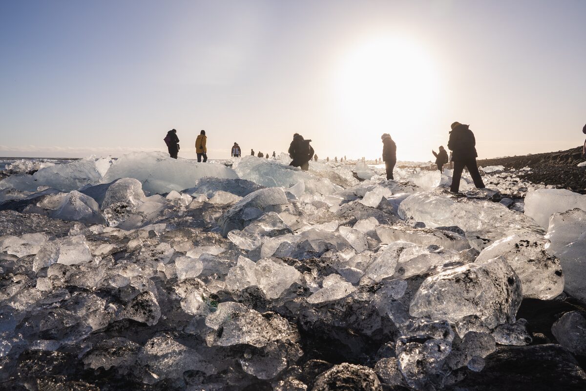 People walking among large iceberg fragments on the black sand of Diamond Beach at sunset, Iceland.