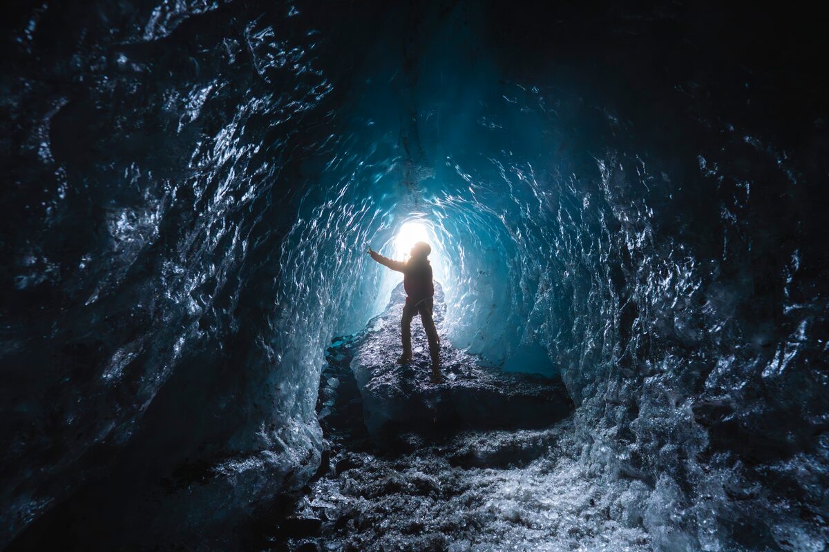 Person silhouetted with a headlamp inside a blue ice cave under Vatnajökull glacier in Iceland, jagged ice floor visible.