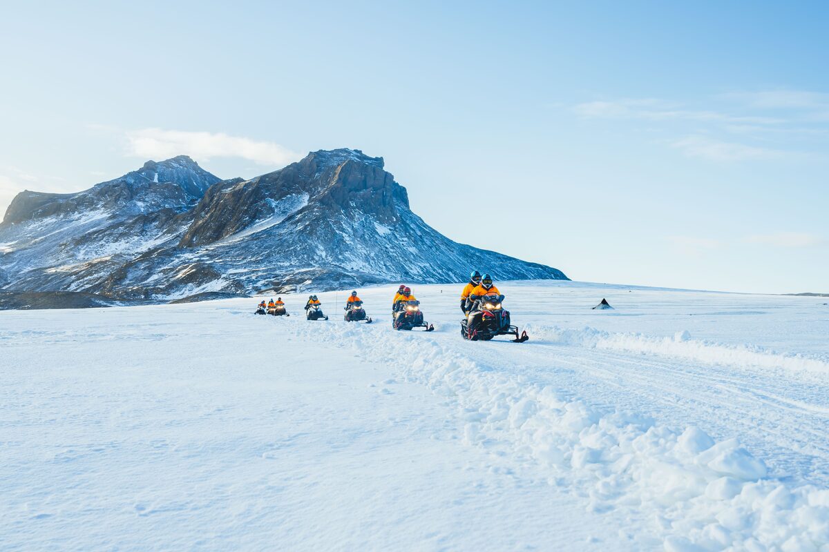 Group of snowmobiles in a line on the snow surface of Langjökull glacier in Iceland, dark mountain ridge behind.