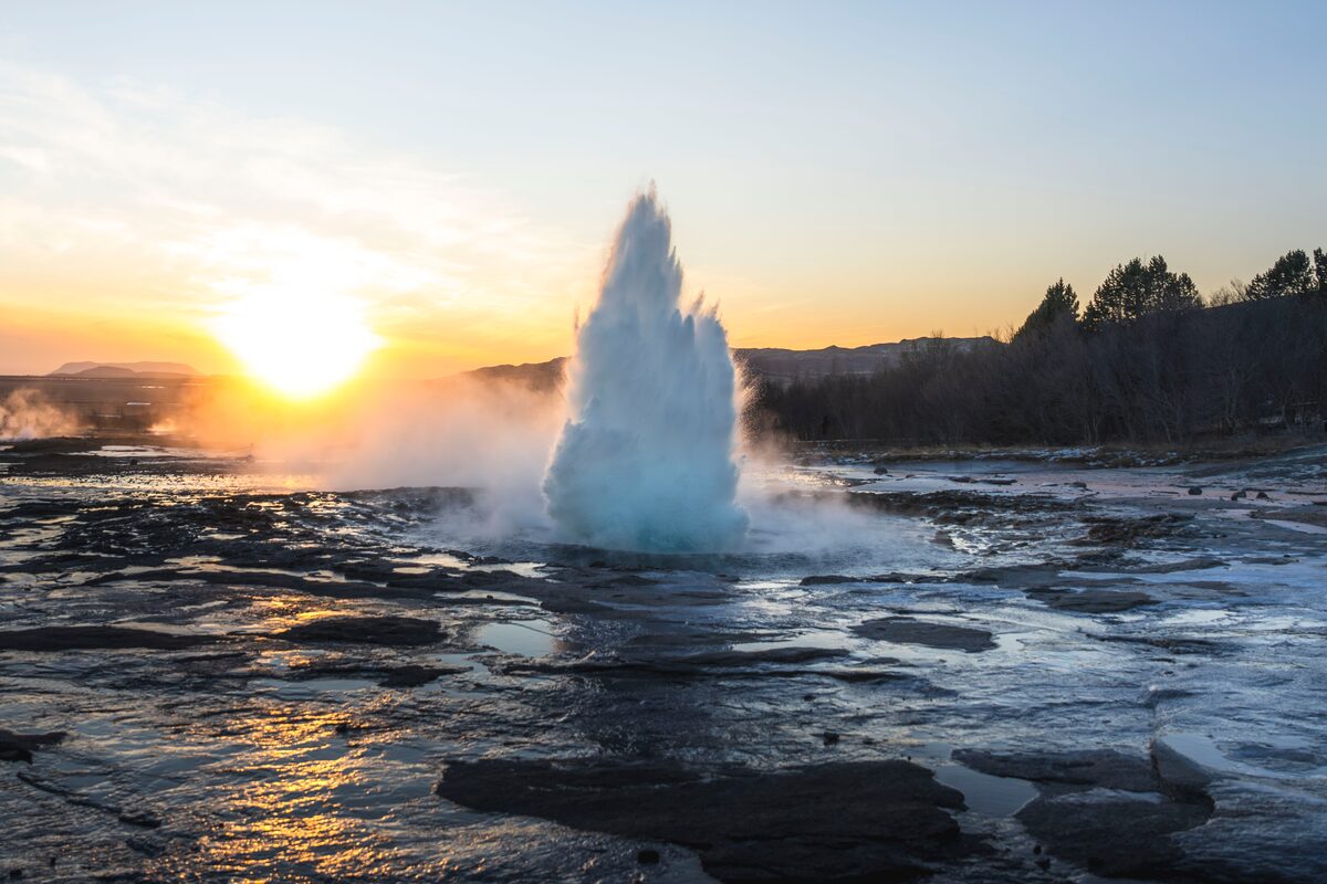 Strokkur geyser erupting at sunset in the Haukadalur geothermal area, Iceland, with steam catching the light.