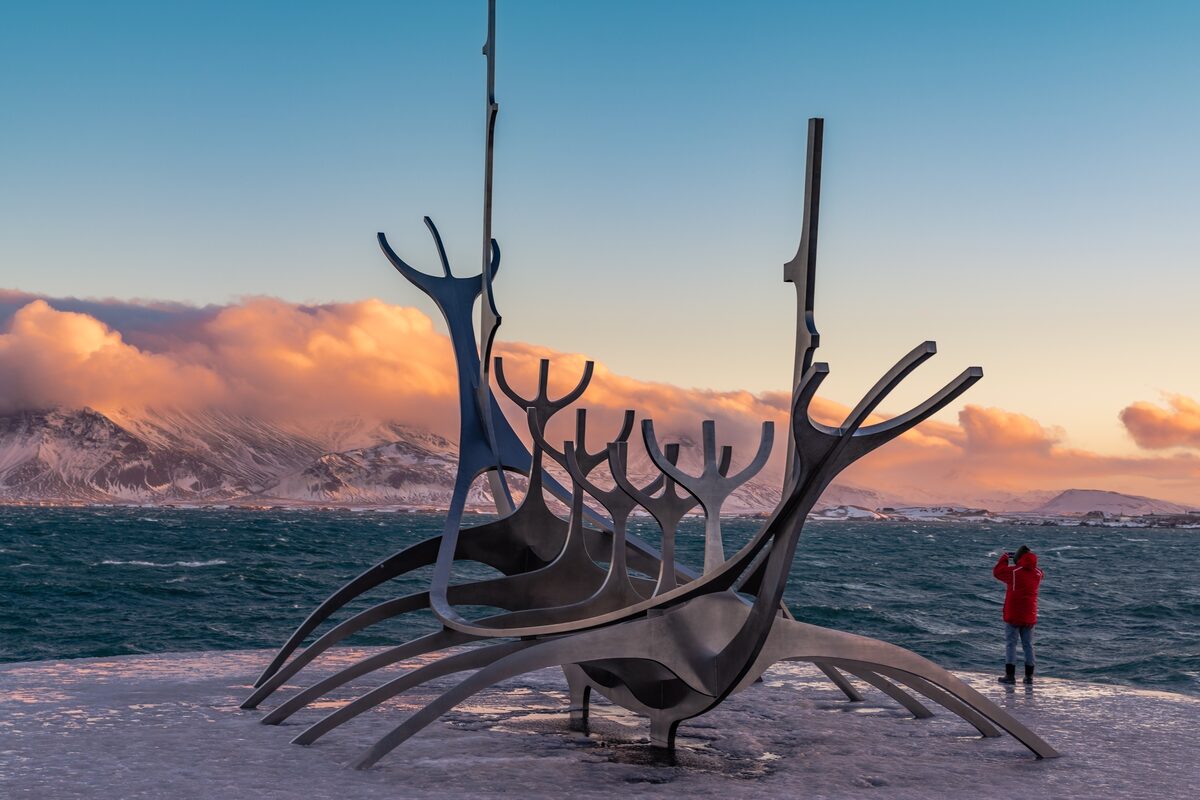 The Sun Voyager sculpture on Reykjavík's shore with mountains and low sun behind.