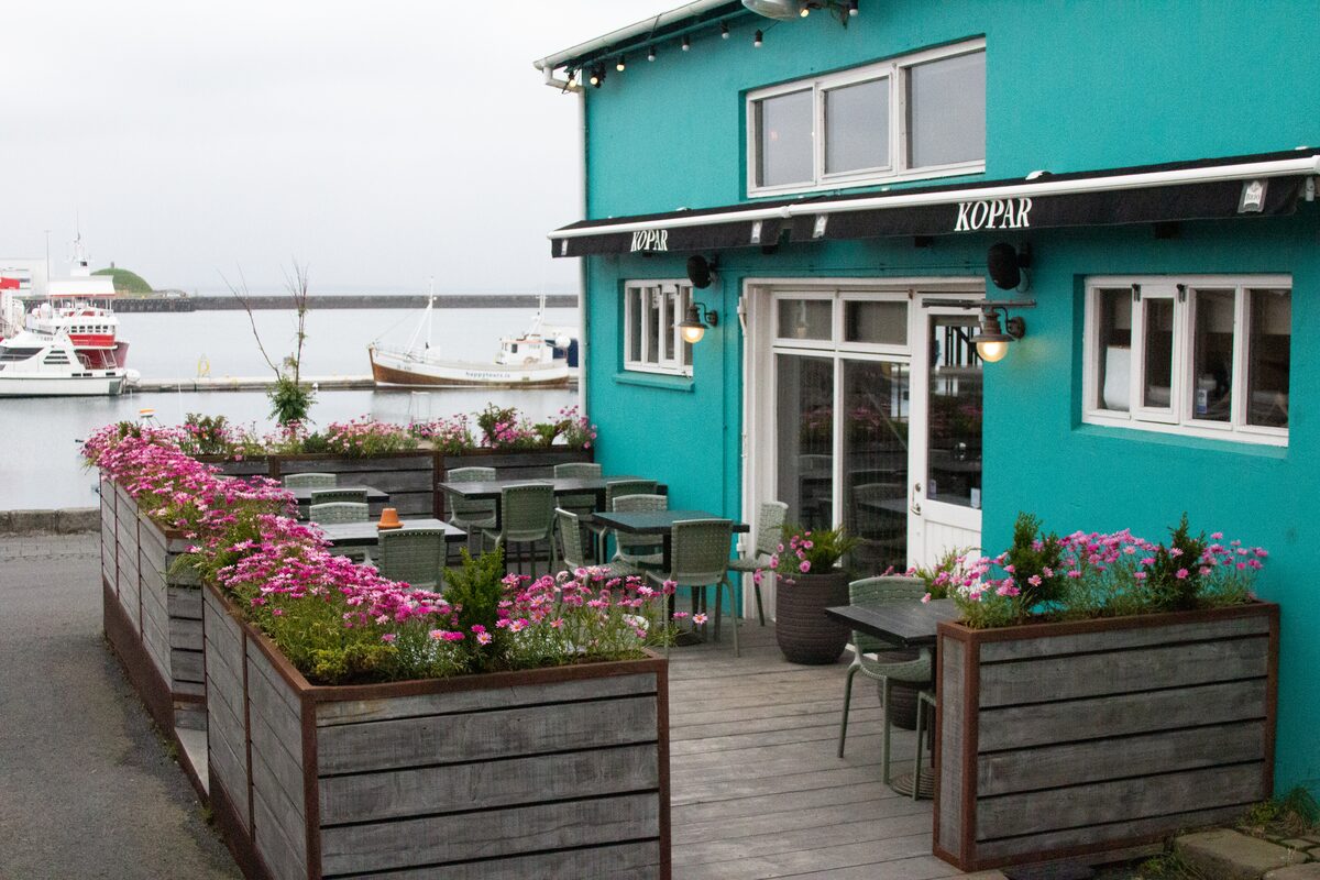 Kopar restaurant with a harbourside terrace, flower boxes and boats behind, in Reykjavík.