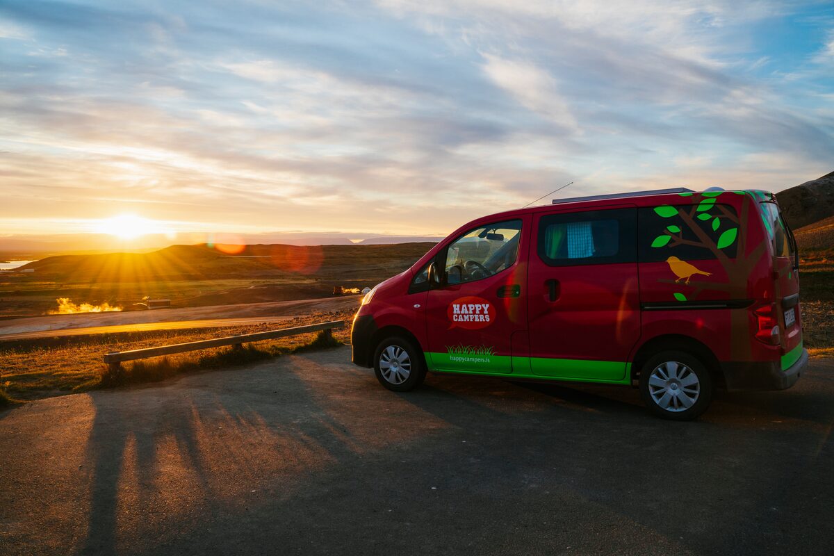 Red campervan parked at a roadside pullout at sunset in the Icelandic countryside.