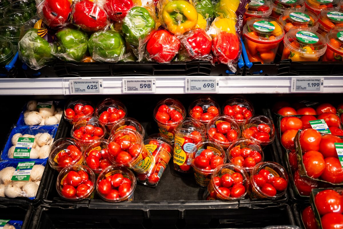 Supermarket shelf of packaged peppers, tomatoes and mushrooms with price tags in Iceland.