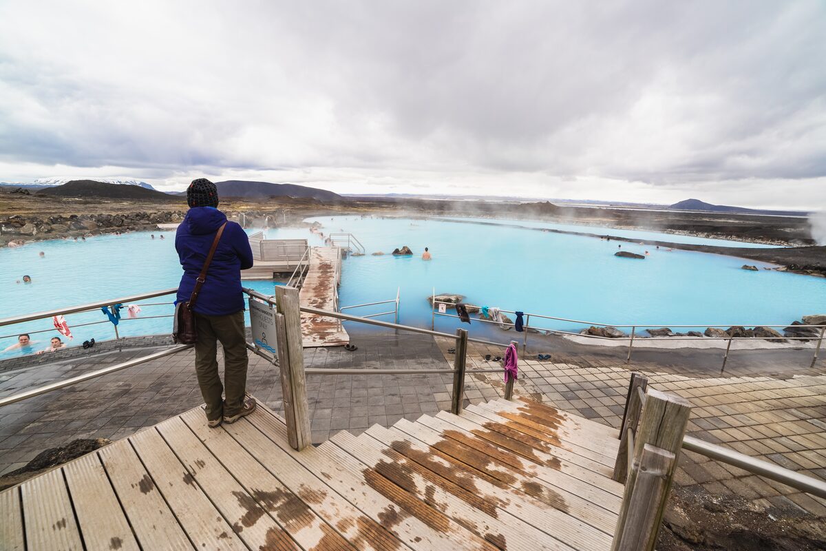 Person on wooden steps looking over the milky-blue Mývatn Nature Baths lagoon and lava field.