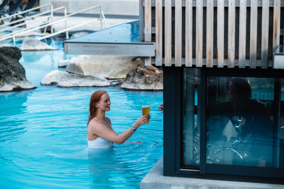 Woman in the lagoon holding a drink at the swim-up bar window at Mývatn Nature Baths.