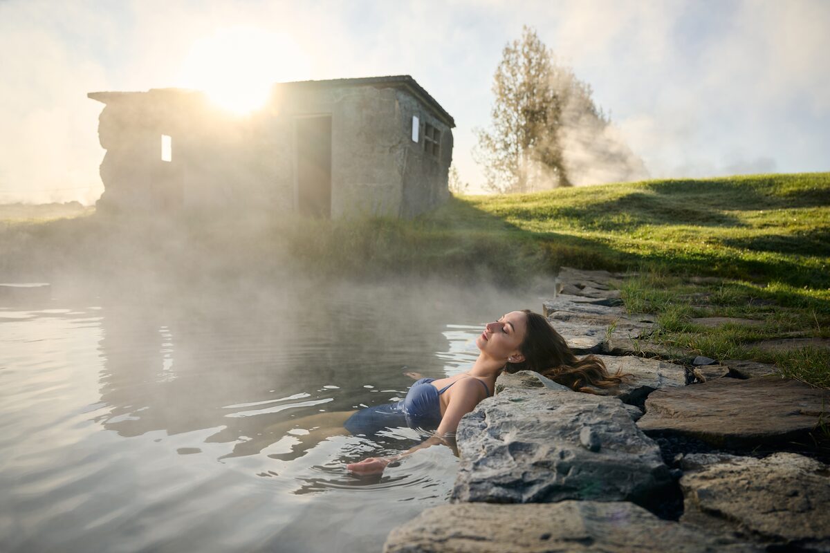 Woman in a blue swimsuit resting by the stone edge of the steaming Secret Lagoon.