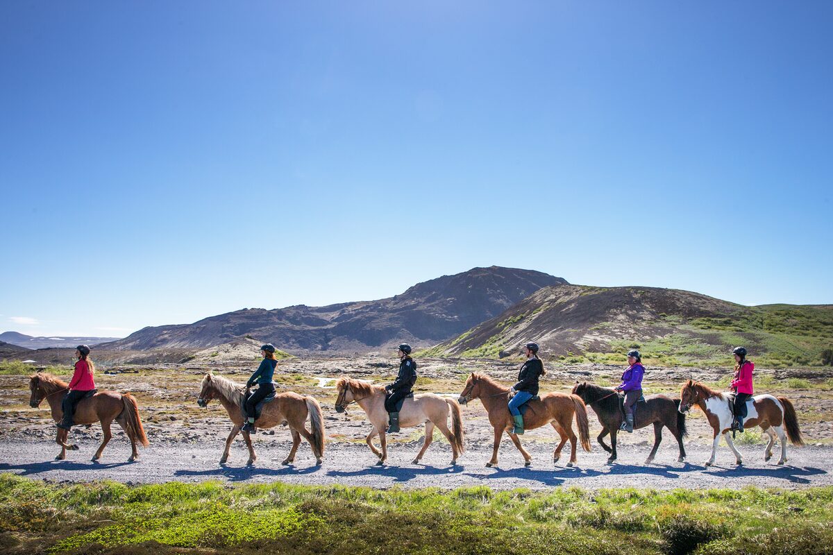 People On Horses Riding In A Line With Mountains In The Background in Iceland