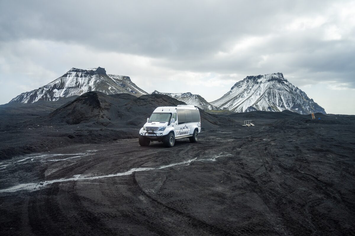 An Arctic Adventures Super Jeep on black volcanic ground in Iceland below snowy mountains.