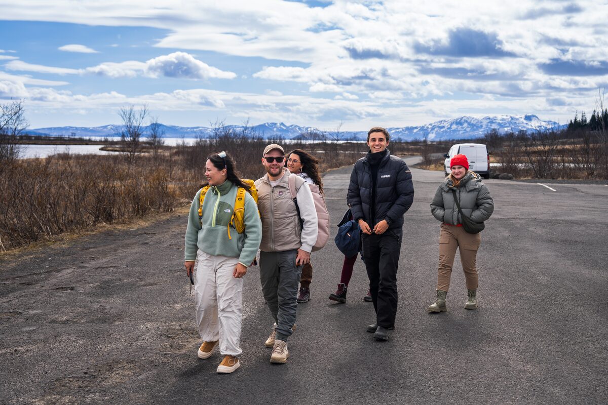 Group of people walking on a road in Iceland with snow-capped mountains behind them.