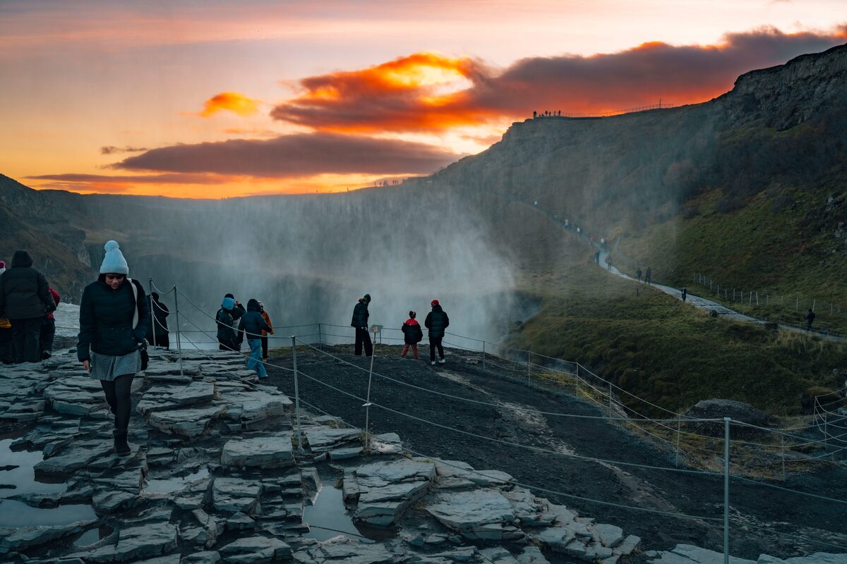 People walking a fenced viewing path above Gullfoss waterfall in Iceland at sunset.