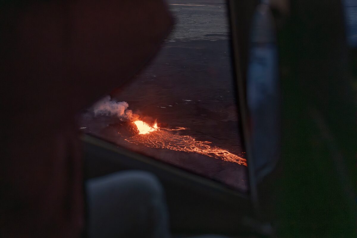 Glowing lava and a plume of smoke erupting from a fissure in Iceland at dusk.