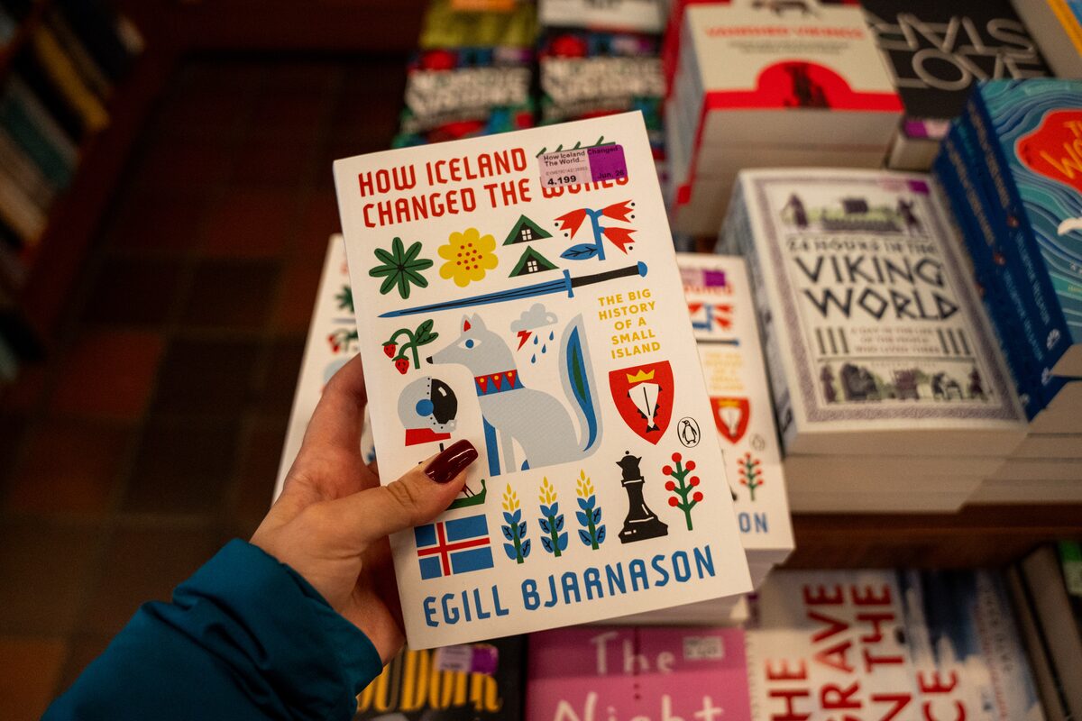Person holds Egill Bjarnason's book How Iceland Changed the World above a bookstore table.