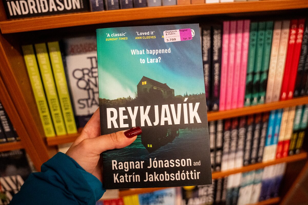 Hand holding the book Reykjavík by Ragnar Jónasson and Katrín Jakobsdóttir in a bookstore.