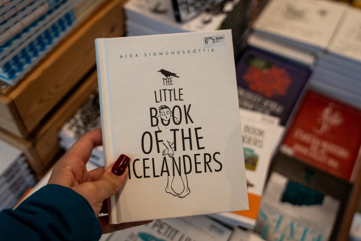 Person holds Alda Sigmundsdóttir's book The Little Book of the Icelanders above a shop display.