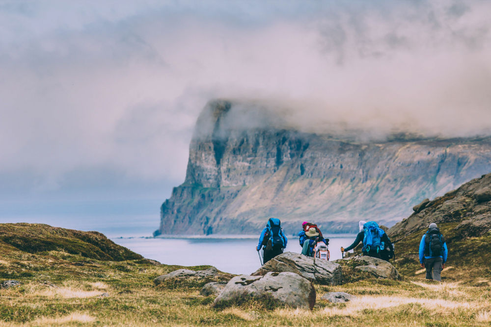 Four Hikers Going Towards The Shore With A Big Cliff In The Background in Iceland