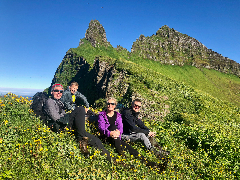 Four People Sitting Near A Green Cliff in Iceland