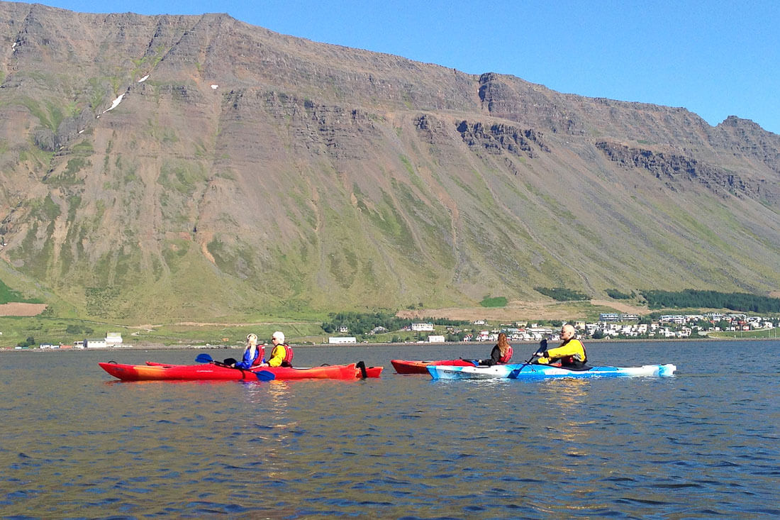Three Kayaks In Water With Town And Mountains In The Background in Iceland