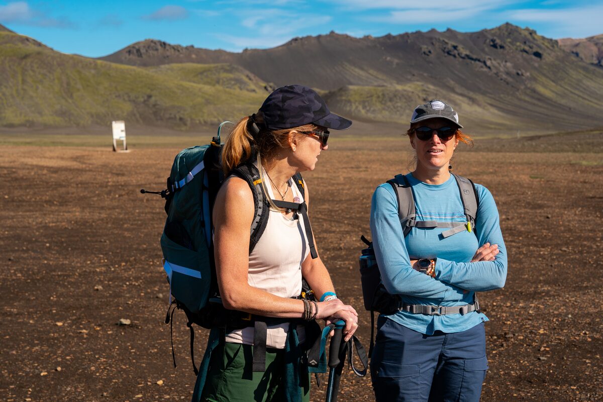Two women hikers with backpacks talking on a trail in the Icelandic highlands in summer.