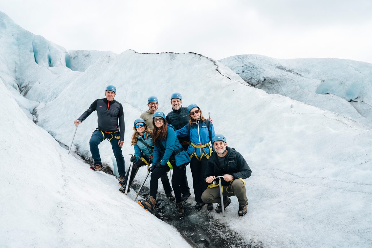 Small group in helmets and harnesses posing with ice axes on a glacier in Iceland.