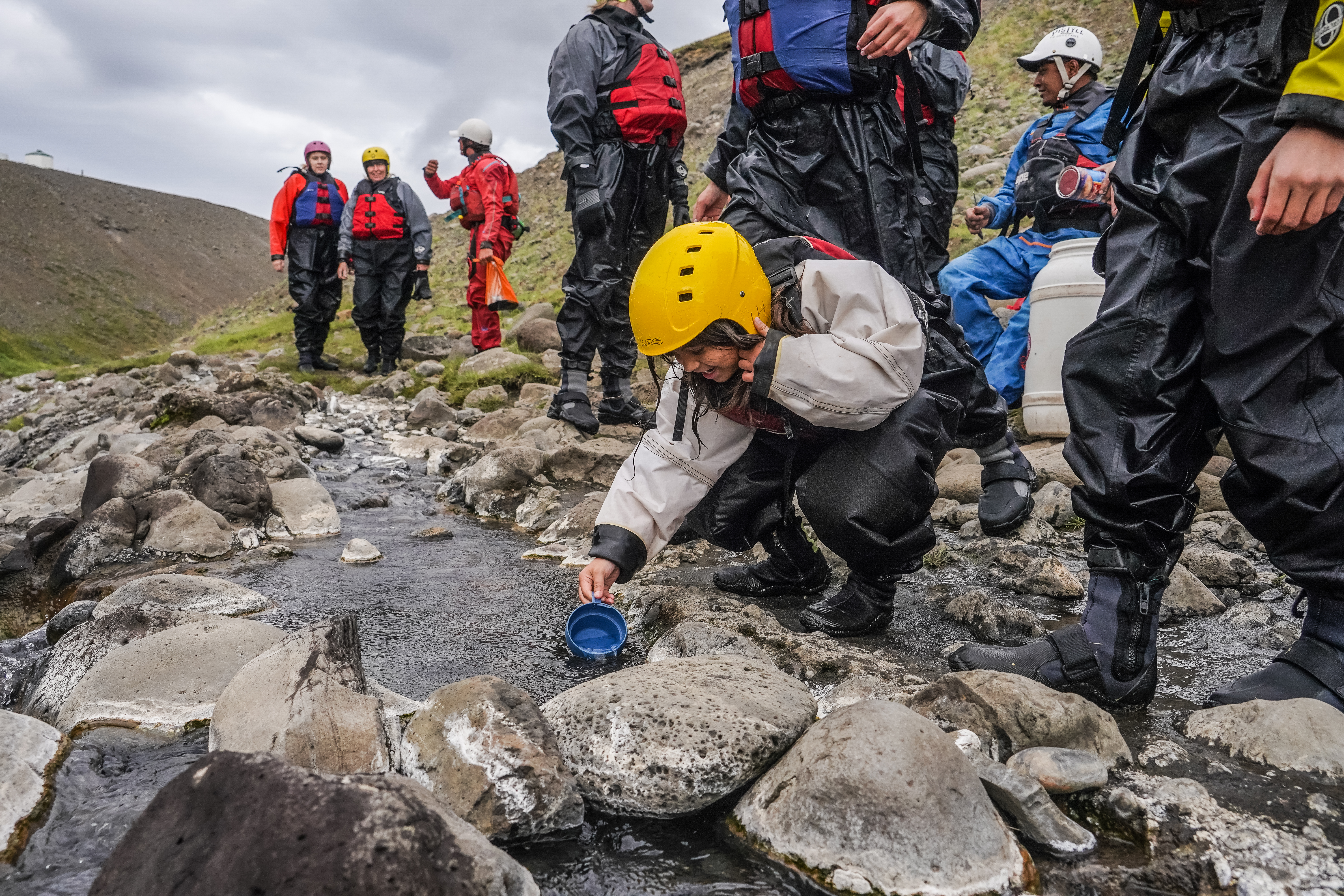 People Near A Stream And Woman Scooping Water in Iceland