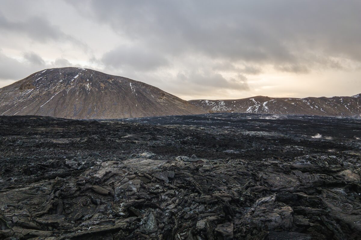 Dark lava field with low mountains under a cloudy sky on the Reykjanes Peninsula, Iceland. 