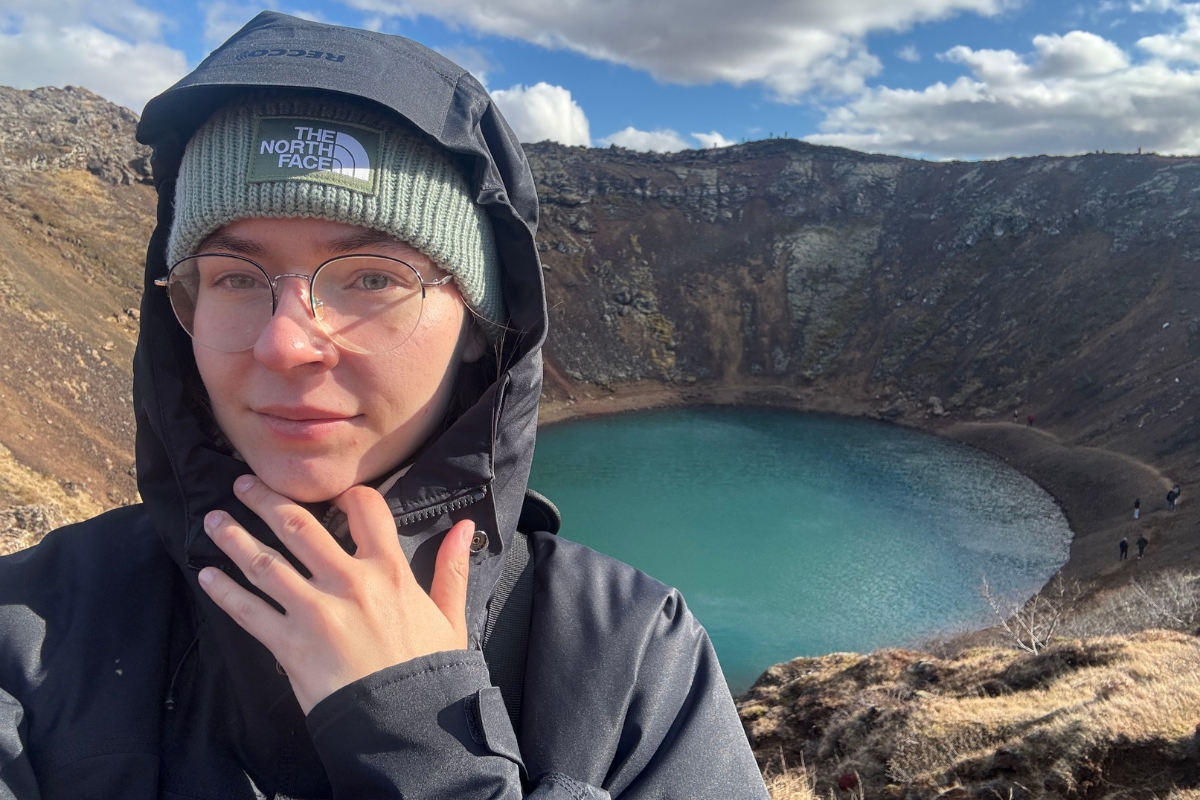 Justyna is taking a selfie at the rim of Kerið crater, with the turquoise crater lake and volcanic walls behind her.