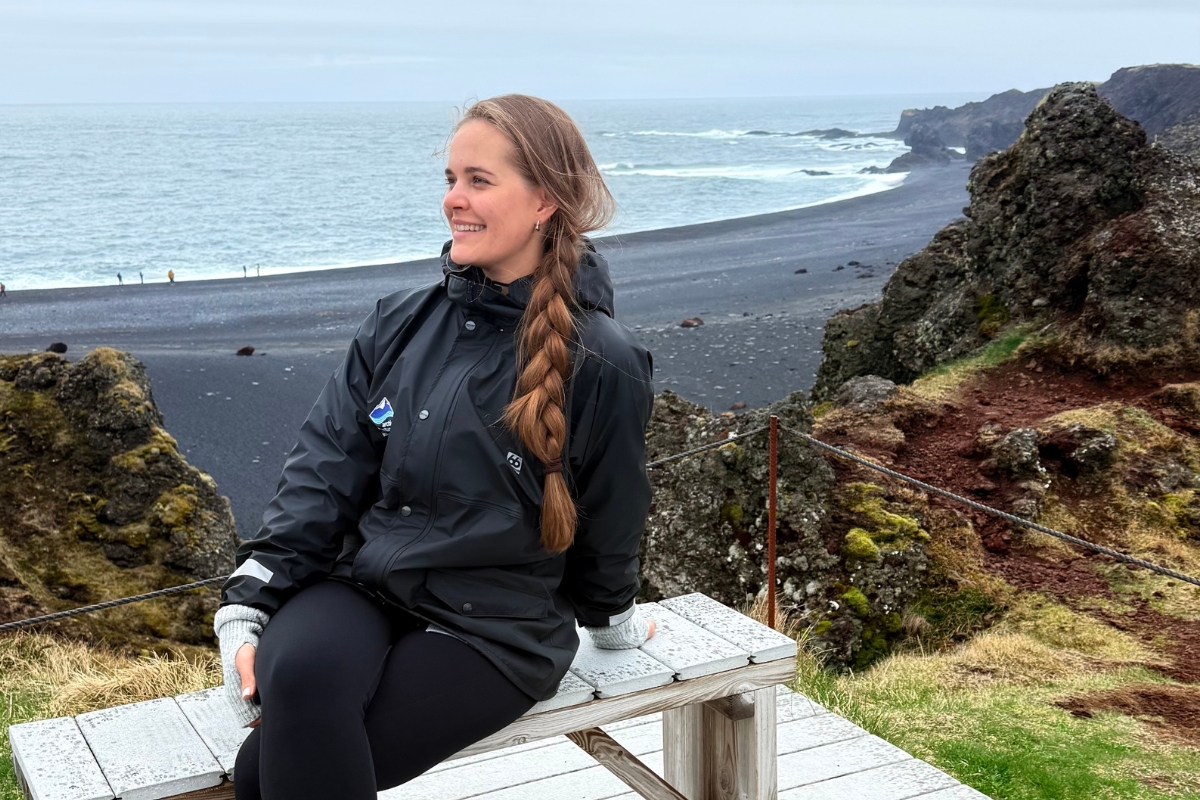 Anhelina Zhaliazka, Content Lead at Arctic Adventures, sitting on a bench at Djúpalónssandur beach in Snæfellsjökull National Park, West Iceland.