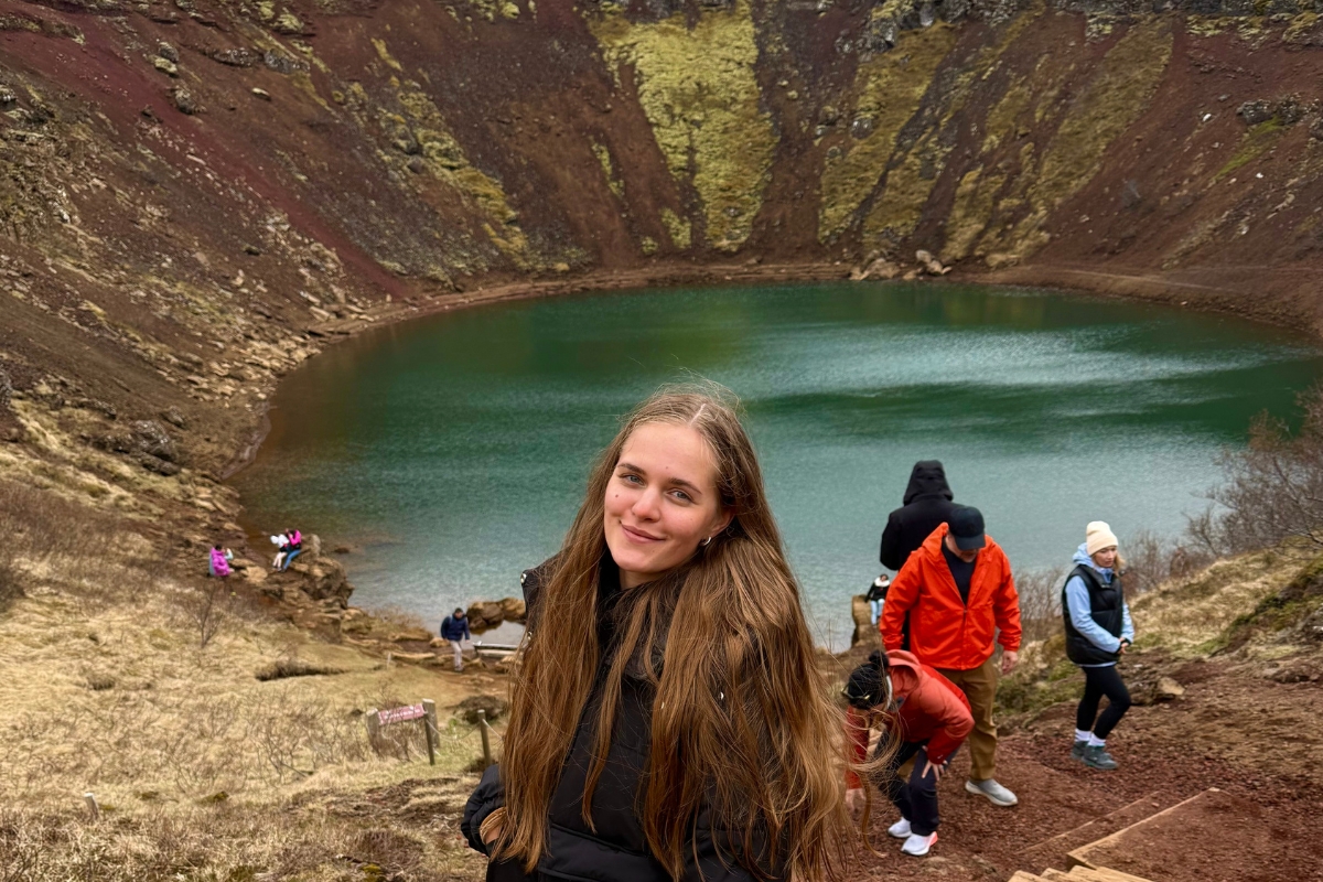 Anhelina on the wooden steps at Kerið crater, the green lake and red volcanic walls behind her on the Golden Circle tour in Iceland.