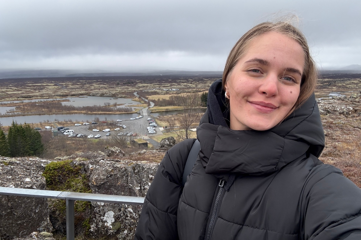 Anhelina Zhaliazka is taking a selfie at Þingvellir National Park, the valley floor and parking area below her on the Golden Circle stop.