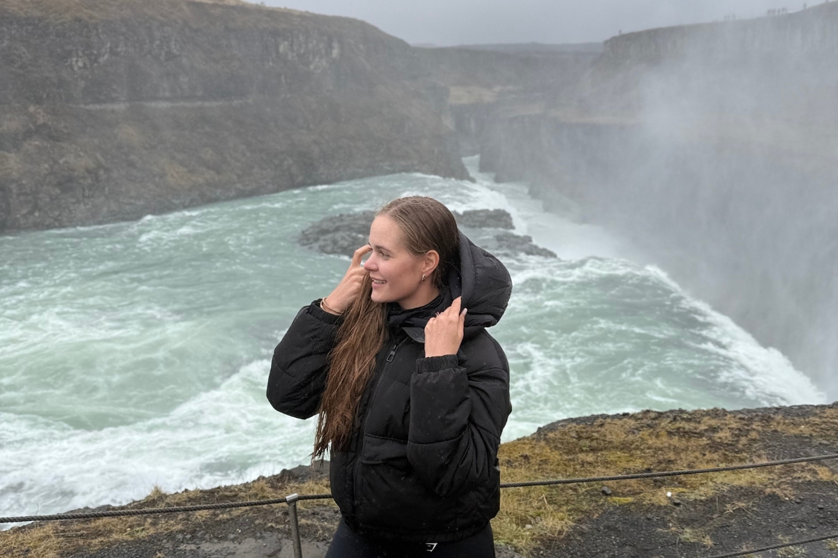 Anhelina Zhaliazka standing by the railing at Gullfoss, mist rising from the falls in the Hvítá canyon behind her.