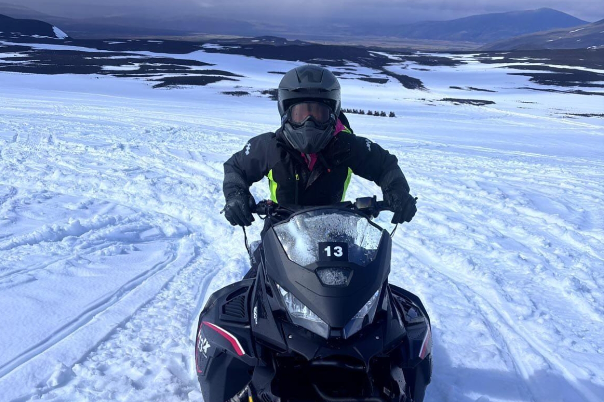 Eva Sadler, Writer and Editor at Arctic Adventures, snowmobiling on Langjökull glacier in a black suit and grey helmet.