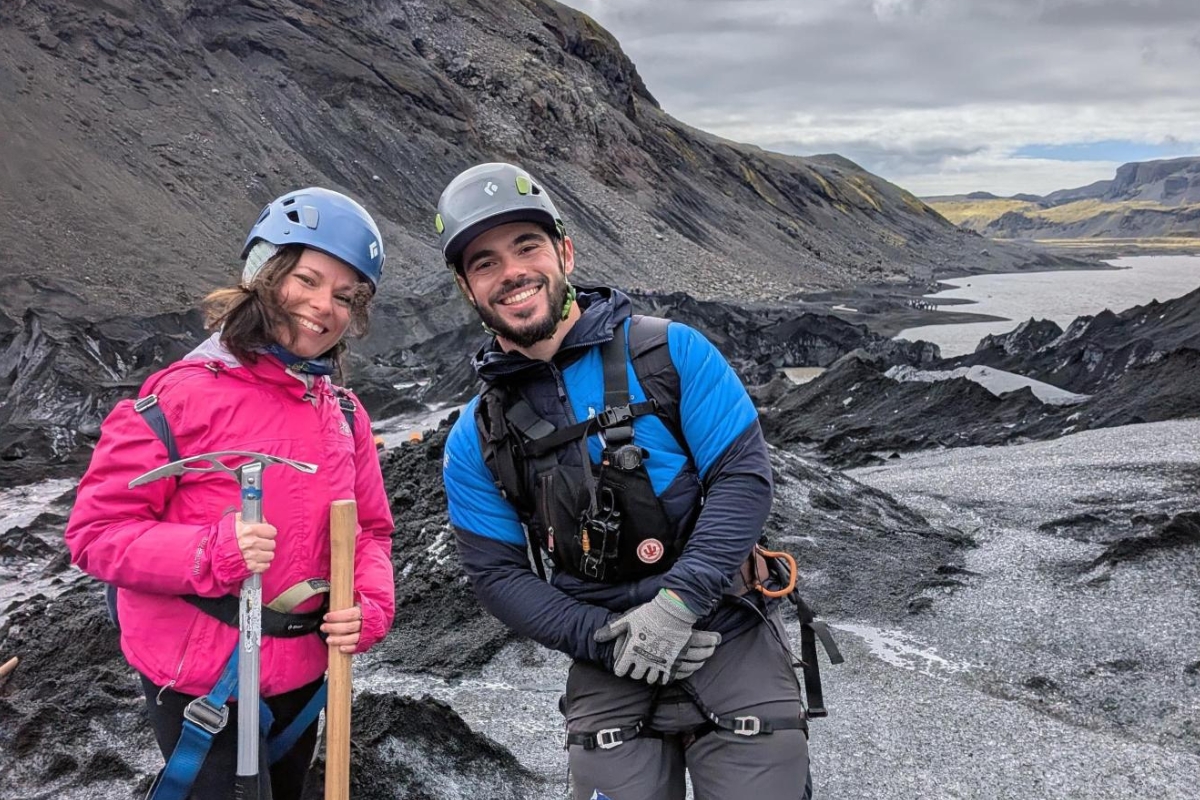Eva Sadler with Arctic Adventures guide Daniel Soares posing on a Sólheimajökull glacier hiking tour with the black ridges behind them.