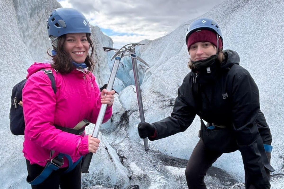 Eva Sadler and a colleague on a Sólheimajökull glacier hike, ice axes raised between blue-grey ice walls.