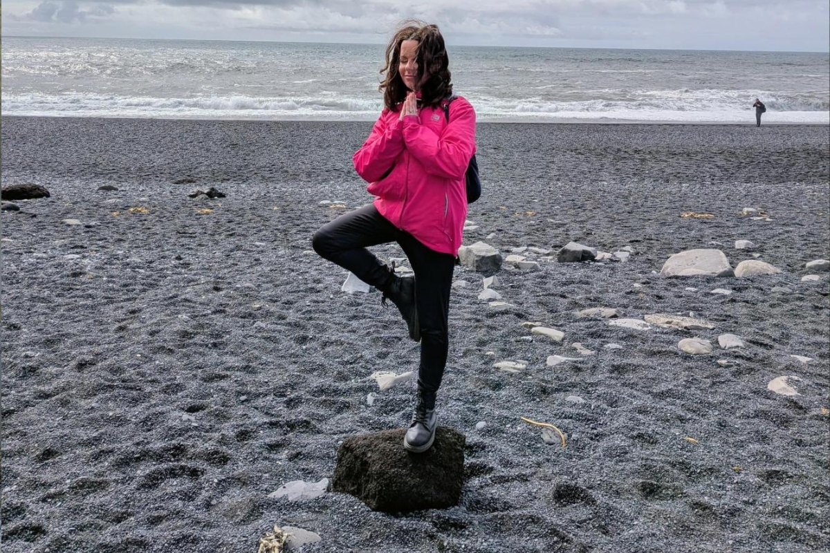 Eva Sadler, Writer and Editor at Arctic Adventures, balancing in a yoga pose at Reynisfjara black sand beach near Vík, South Iceland.