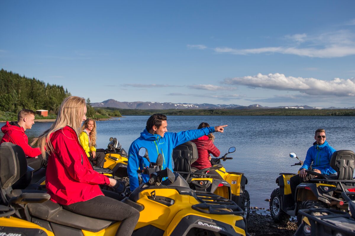 Group on yellow ATVs beside a calm lake as a guide points over the water in Iceland.