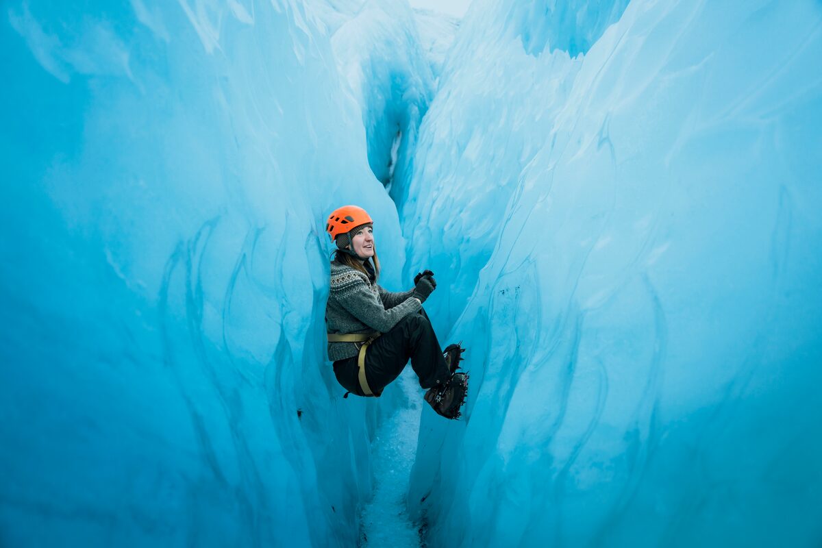 Woman Squating With Her Legs And Back Leaning On Glacier Walls in Iceland