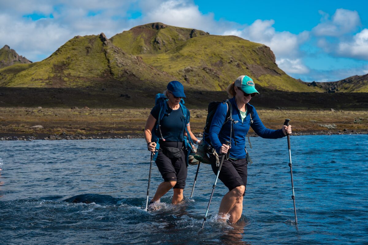 Two Women Wading Through Water While On A Hike At Landmannalaugar in Iceland