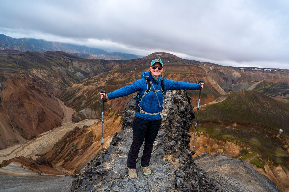 Woman Standing On A Rock Formation With Rhyolite Mountains Around Her in Iceland