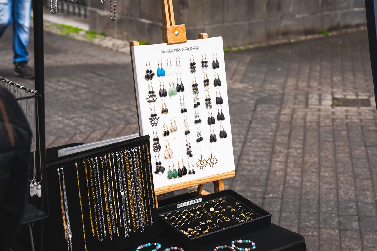 Earrings on a display board with trays of rings and necklaces at an outdoor market stall.