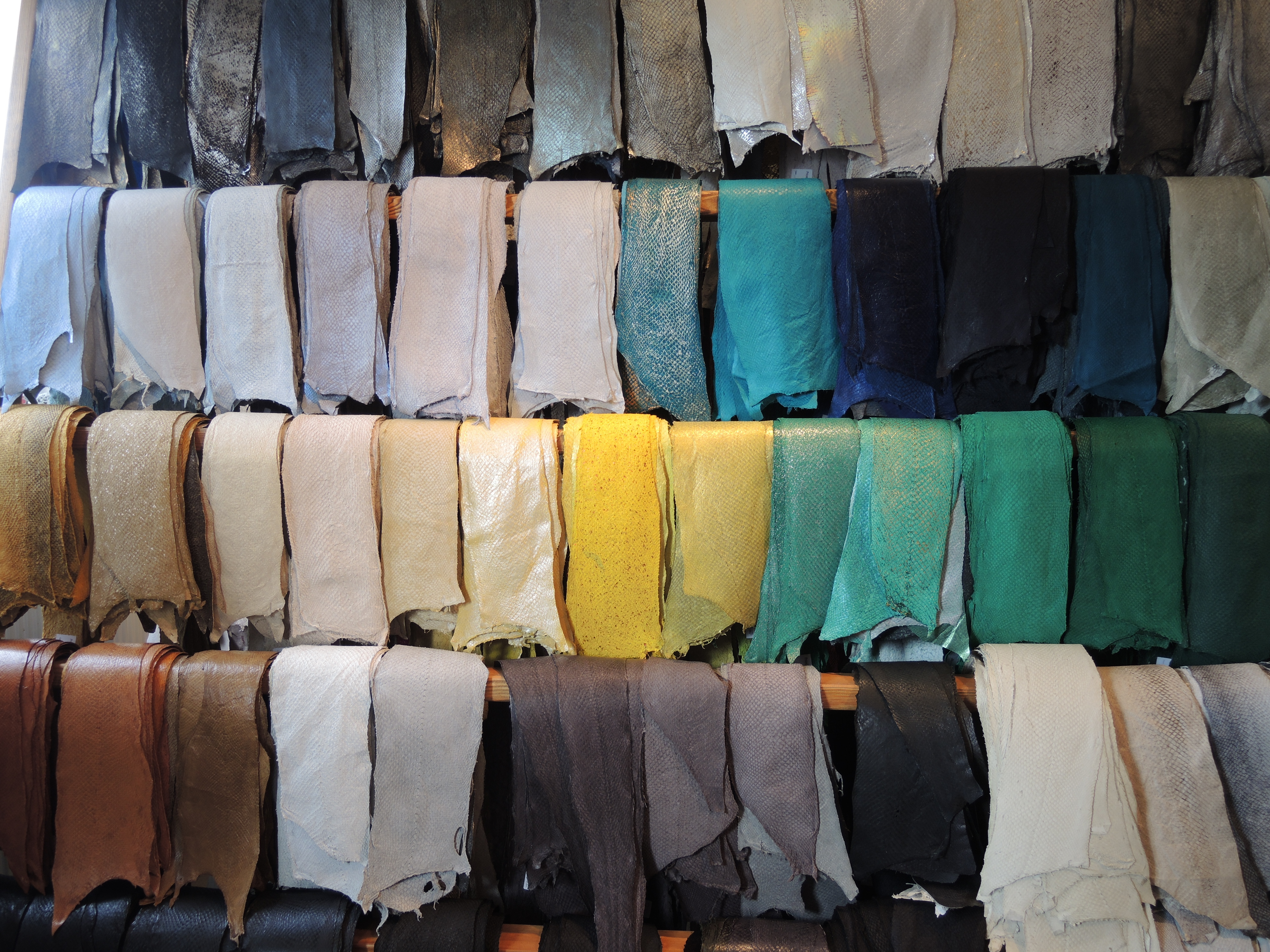 Rows of dyed leather in many colors hanging on wooden racks.