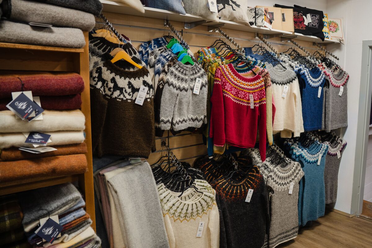 Rack of yoke-patterned wool sweaters in natural and dyed colors beside shelves of folded knits.