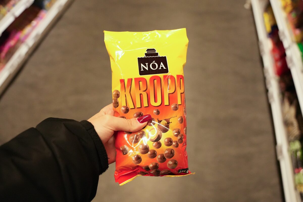 Hand holding a yellow and orange bag of Nóa Kropp candy in a supermarket aisle.