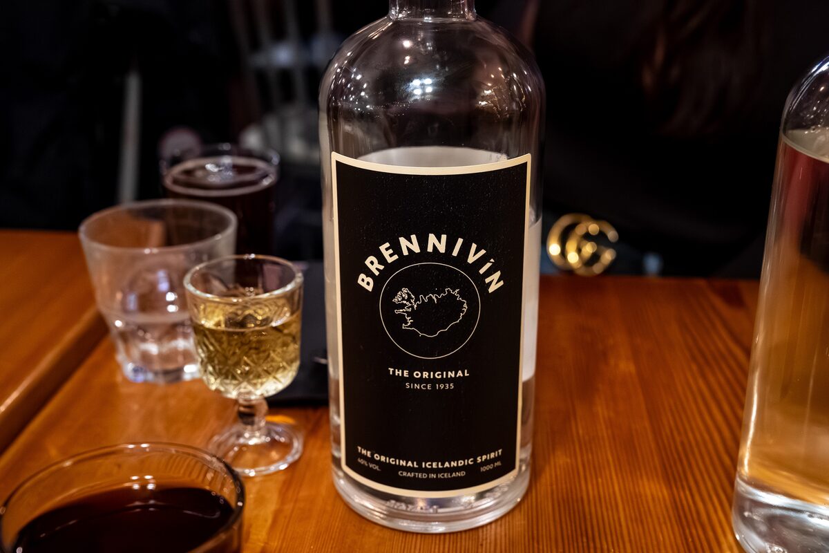 Bottle of Brennivín with a filled shot glass on a wooden table.
