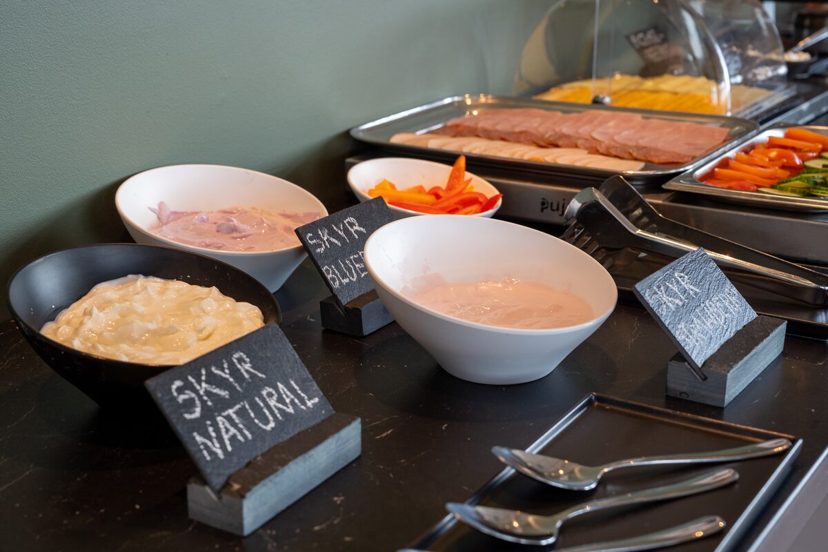 Bowls of natural and blueberry skyr with smoked meat and vegetables on a breakfast buffet.